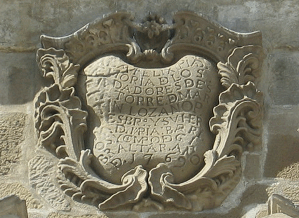 Escudo: broquel de 1769 en memoria de los fundadores de la iglesia y que menciona ya al Campo de Gibraltar